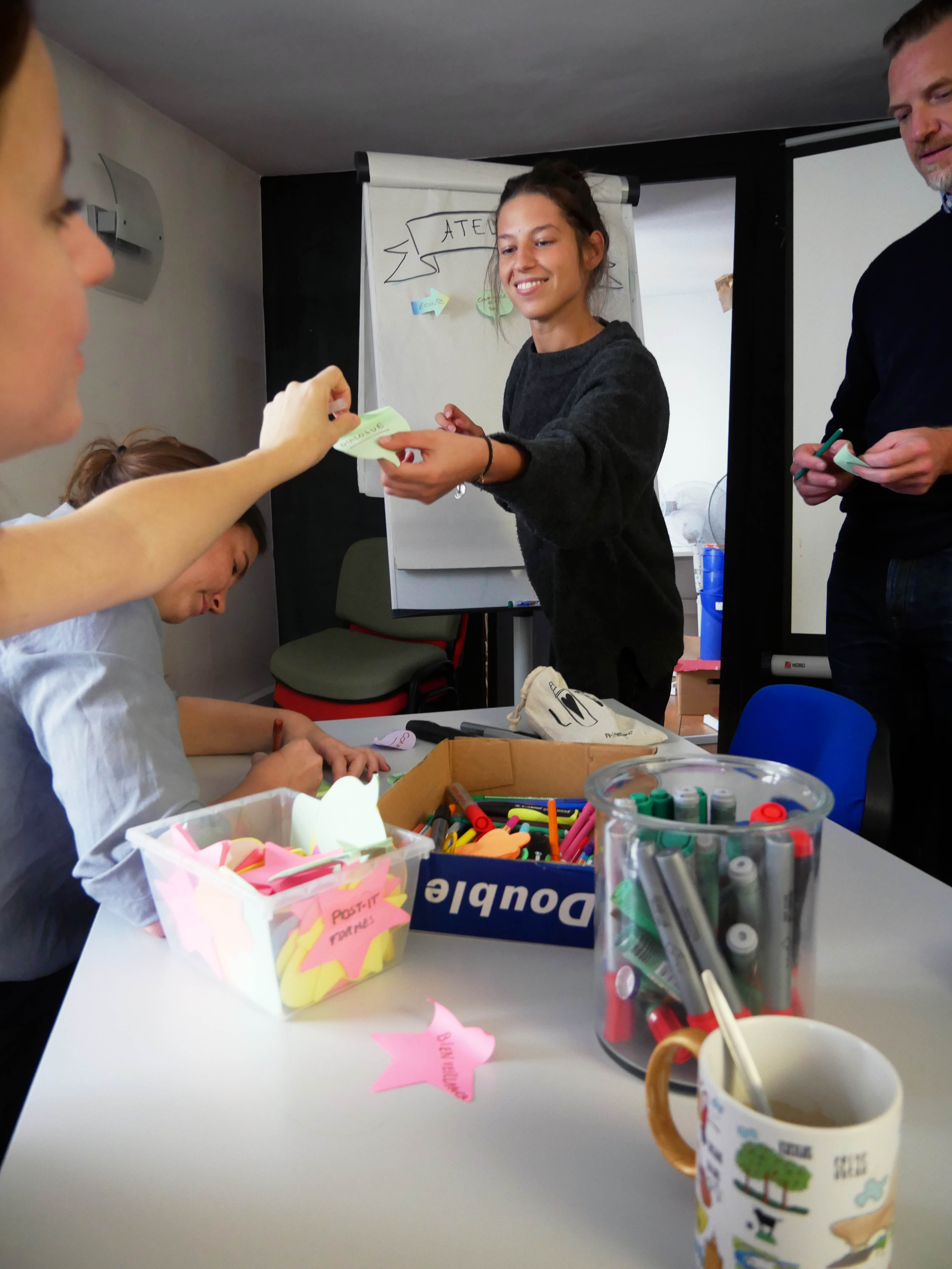 Photo représentant un atelier participatif. Une personne tend un post-it à l'animatrice.